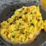 Soft Scrambled Eggs on bread sitting next to a glass of orange juice.