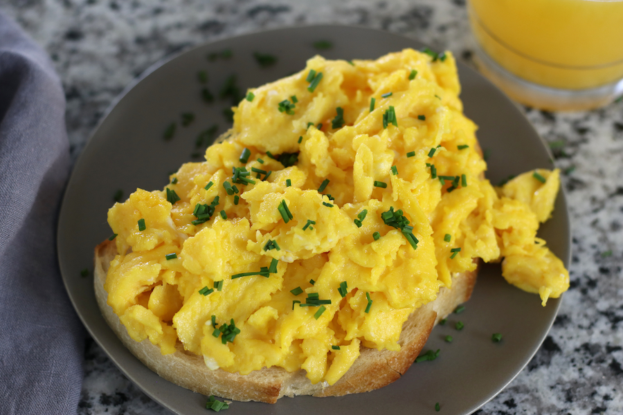 Soft Scrambled Eggs on bread sitting next to a glass of orange juice.