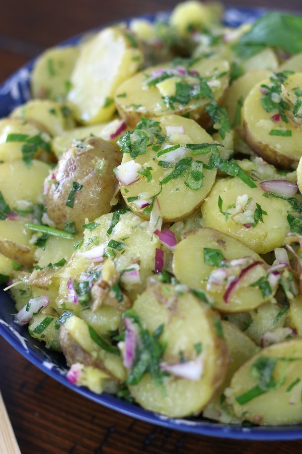 Potato Salad without mayo served in a blue bowl with red onions and fresh herbs.
