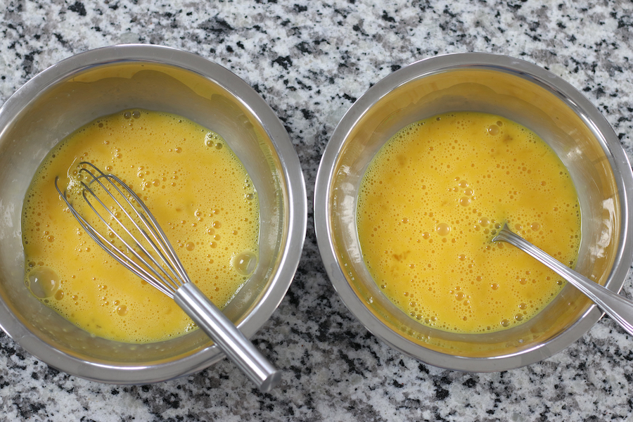 Two bowls of beaten scrambled eggs. One bowl scrambled with a fork and one bowl with a whisk.