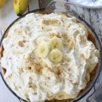 Overhead photo of a Banana Cream Pie sitting on a wooden table.