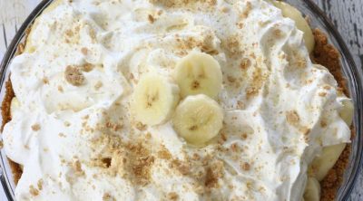 Overhead photo of a Banana Cream Pie sitting on a wooden table.