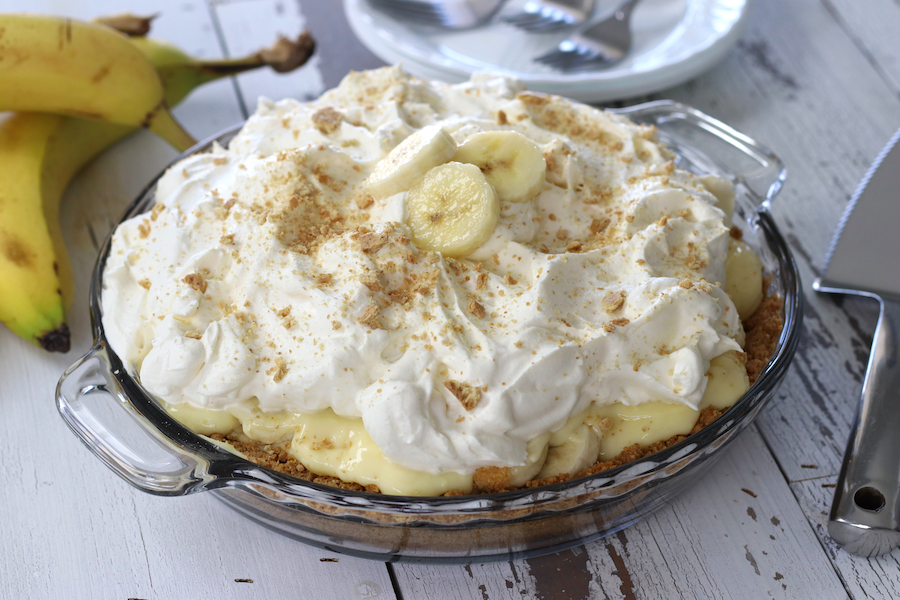 Banana Cream Pie with Graham Cracker Crust sitting next to plates and a pie server.