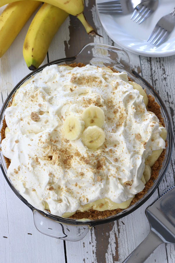 A whole Homemade Banana Cream Pie with fluffy homemade whipped cream sitting on a table.