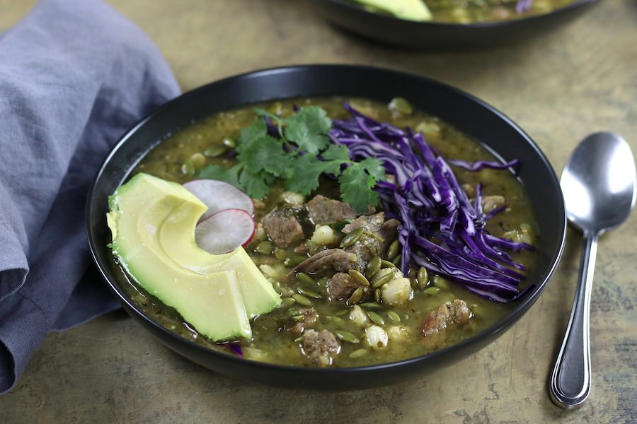 A bowl of Pork Pozole Verde Recipe sitting on a table top next to a spoon and napkin.