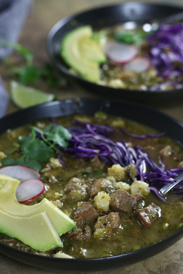 Pozole Verde garnished with avocado, radish slices and shredded red cabbage.