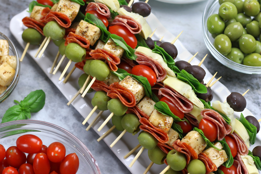 Antipasto Skewers recipe prepared on a white rectangle platters surrounded by bowls of olives and tomatoes.