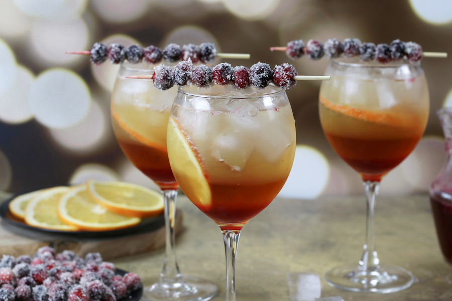 Three Holiday Spritz cocktails sitting on a table in front of Christmas lights.