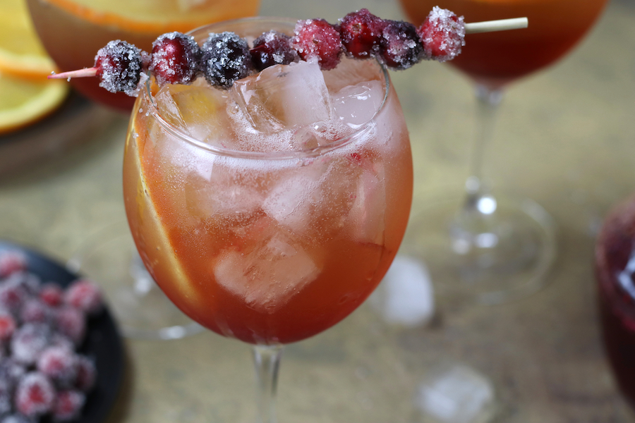 A fizzy Orange Cranberry Cocktail with a slice of orange and sugared cranberries on a toothpick.