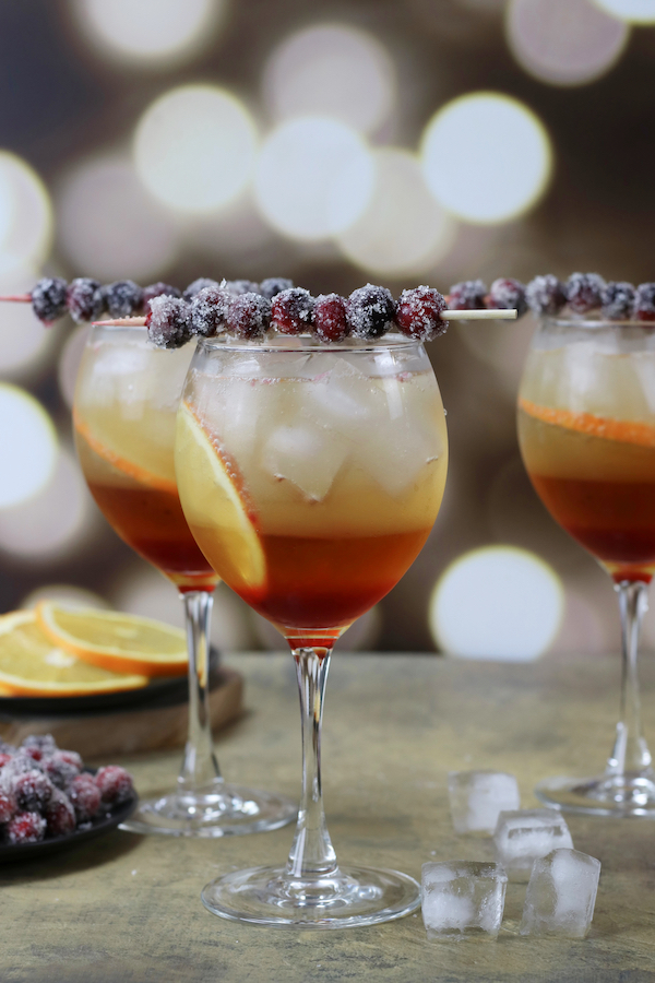 Three Winter Spritz Cocktails in front of out of focus Christmas lights.