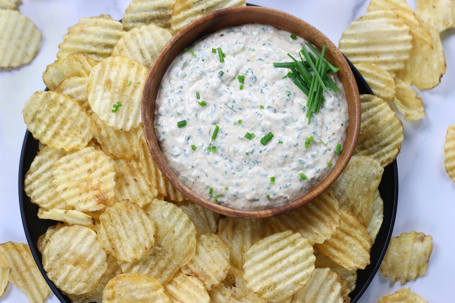 Homemade Garlic Dip served in a bowl with potato chips on a black plate.