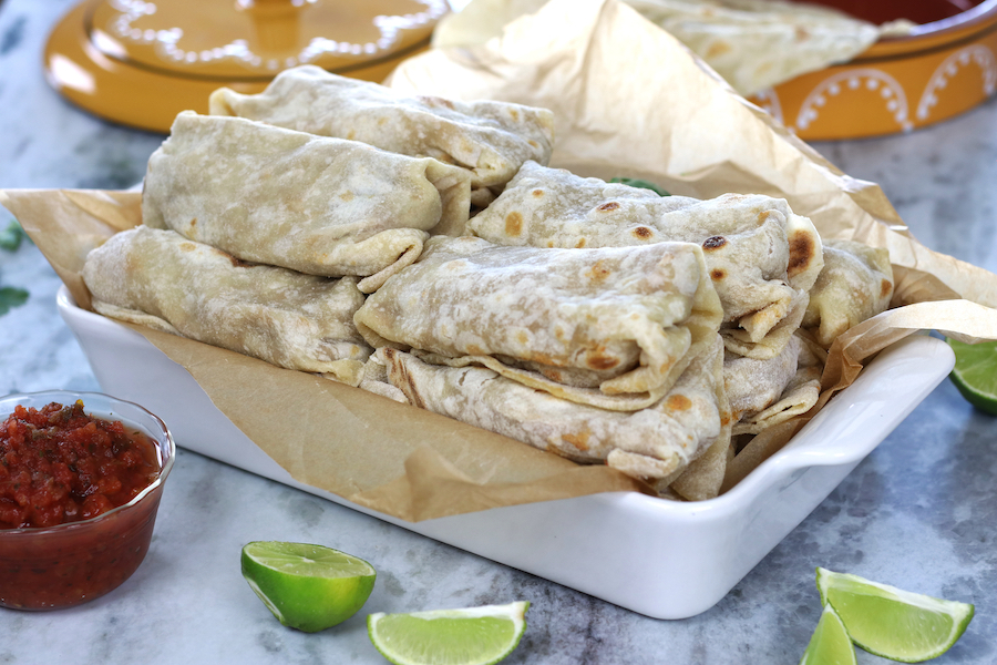 Beef and Bean Burritos piled in a white roasting pan sitting on a marble countertop.