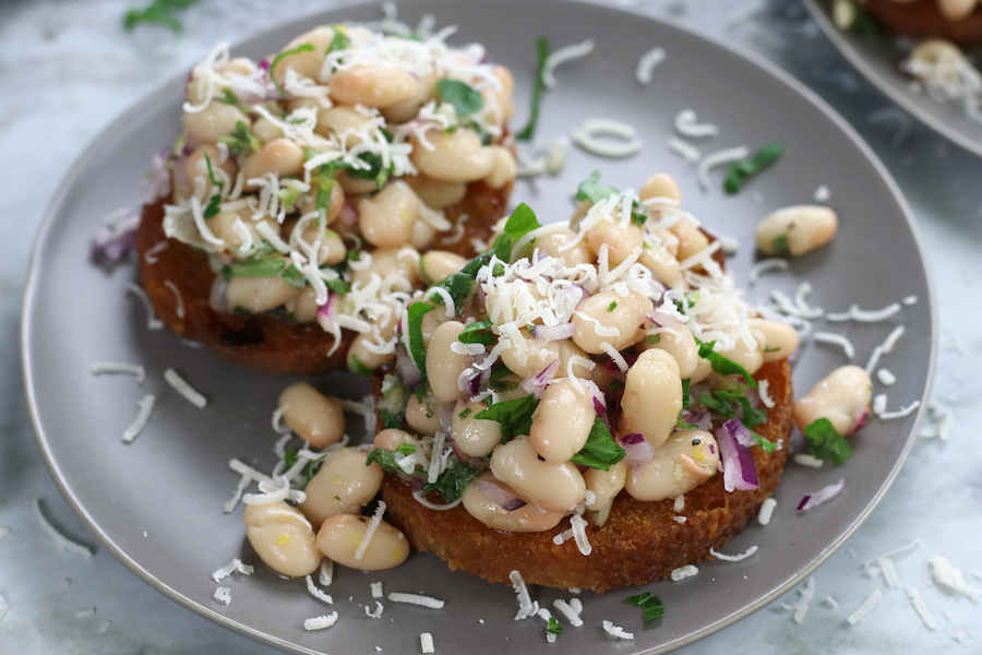 Italian Marinated White Beans served on small pieces of toast and garnished with parmesan.