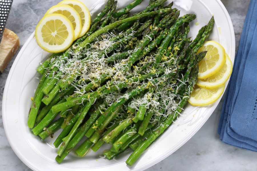 Oven Roasted Asparagus with Garlic, Parmesan and lemon platted on a white platter sitting on a marble countertop.