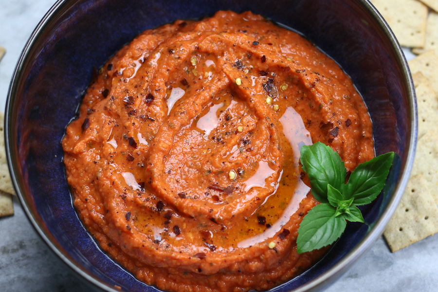 Red Pepper Spread made with roasted bell peppers in a bowl surrounded with crackers.