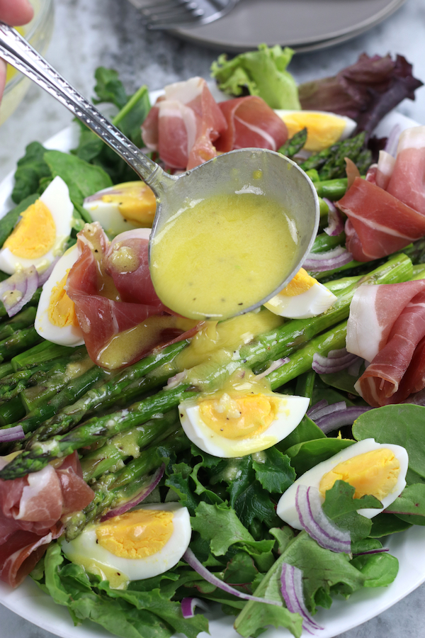 A label of dressing being poured on Asparagus Salad Recipe with hard boiled eggs and prosciutto.