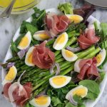 Overhead photo of Asparagus Salad with Egg and Prosciutto on an oval white platter.