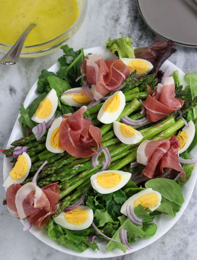Overhead photo of Asparagus Salad with Egg and Prosciutto on an oval white platter.