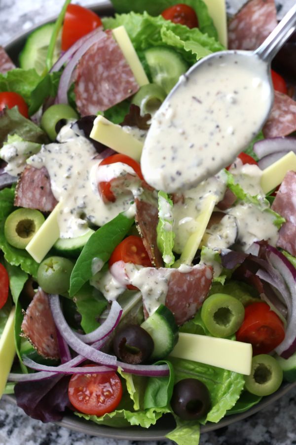 A big plated salad being dressed with Creamy Italian Dressing Recipe.