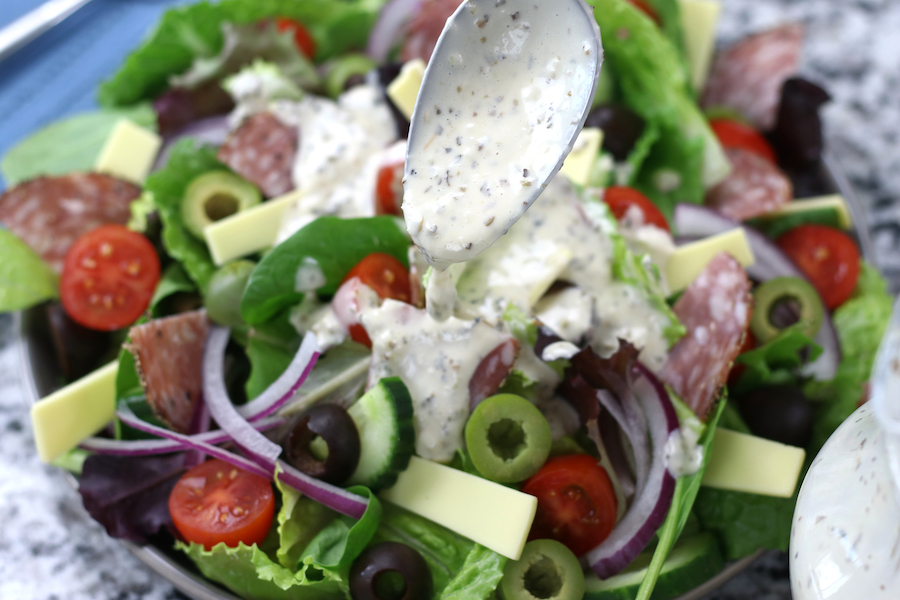 Homemade Creamy Italian Dressing being drizzled over an Italian salad.