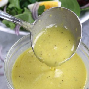 Lemon Mustard Dressing being spooned with a salad sitting behind it.
