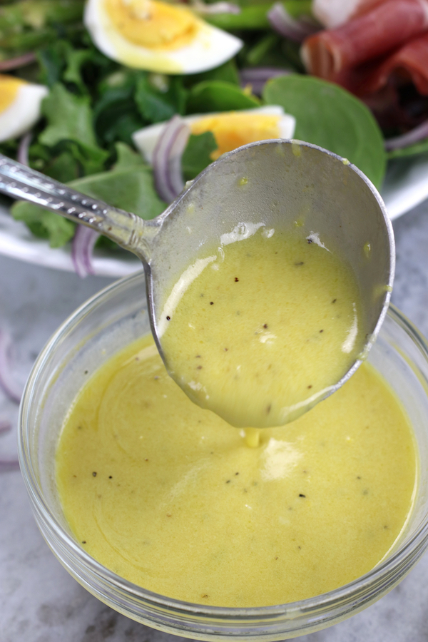 Lemon Mustard Dressing being spooned with a salad sitting behind it.