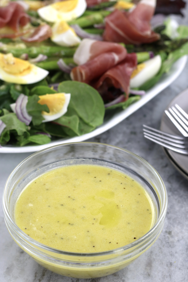 Salad Dressing made of Lemon and Mustard in a small bowl sitting in front of a salad.