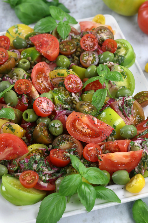 Up close photo of Summer Tomato Salad garnished with Italian olives and fresh basil leaves.