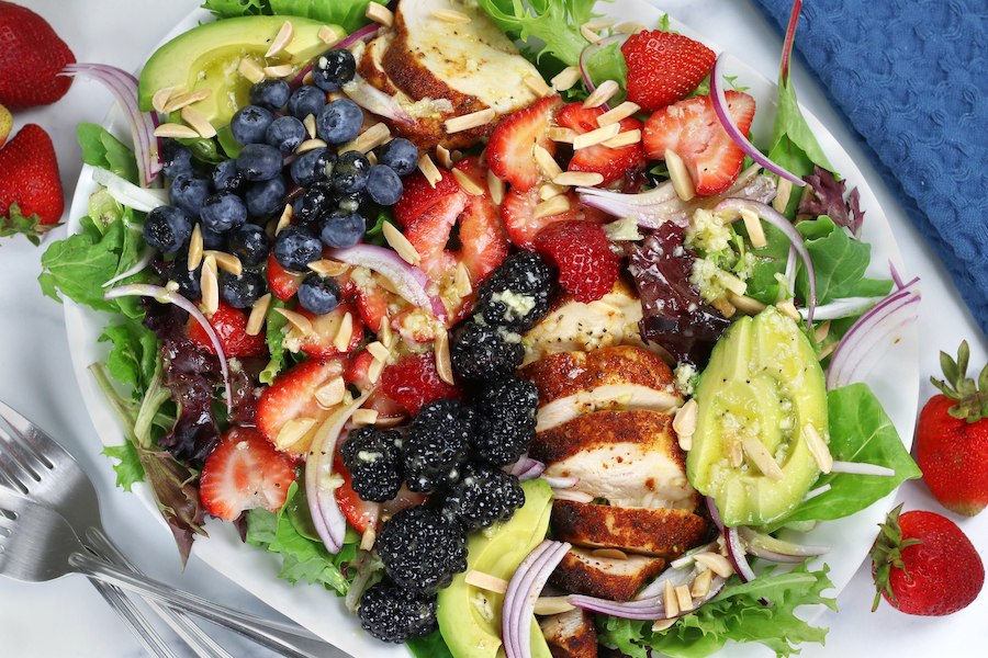 Overhead photo of Triple Berry Chicken Salad on a white platter sitting next to a blue cloth napkin.