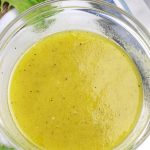 A bowl of White Balsamic Dressing on a white countertop surrounded by a few lettuce leaves.