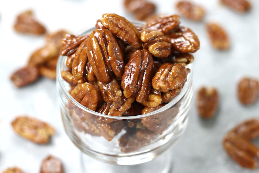 Up close photo of Candied Maple Pecans in a glass parfait cup surrounded by loose pecans.