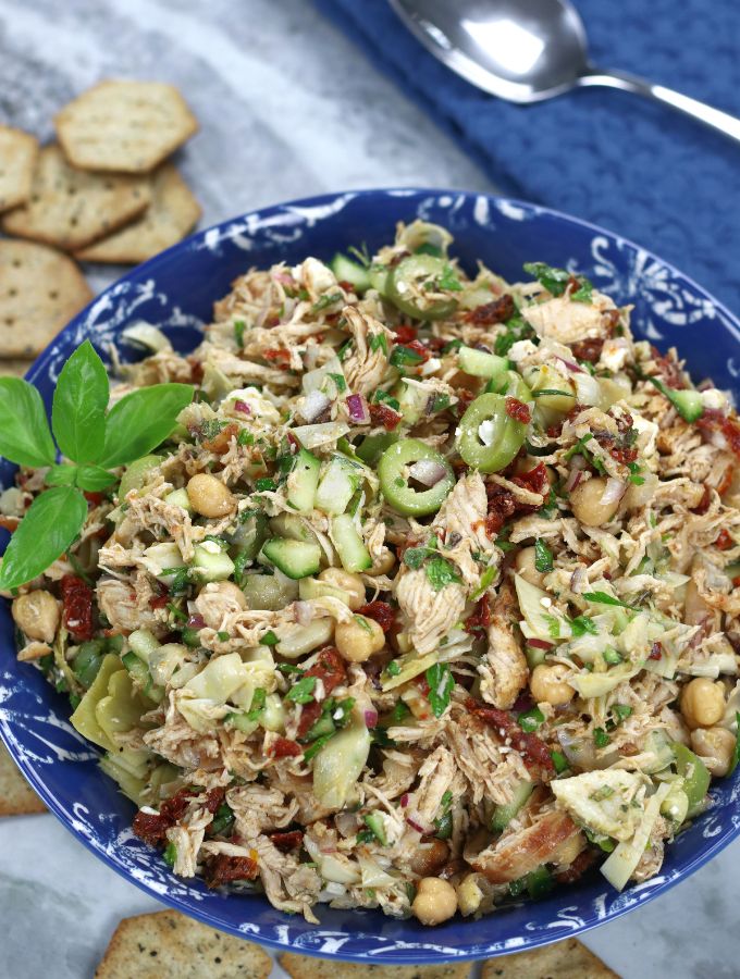 Mediterranean Chicken Salad Sandwich filling in a blue bowl garnished with basil leaves.