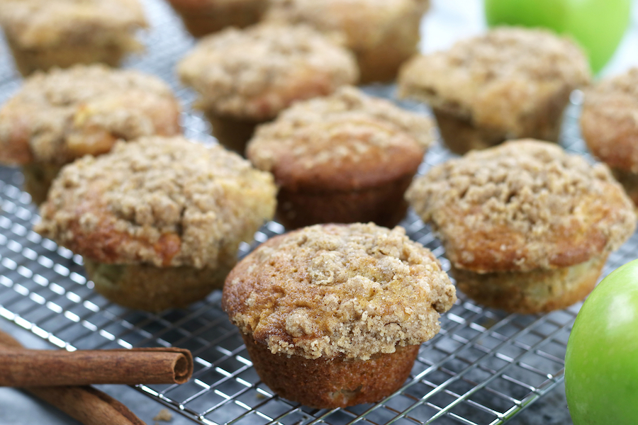 Several Apple Crumb Muffins sitting next to cinnamon sticks and Granny Smith apples.