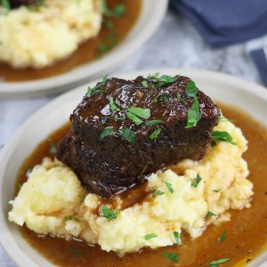 Two plates of Wine Braised Short Ribs garnished with Italian parsley.