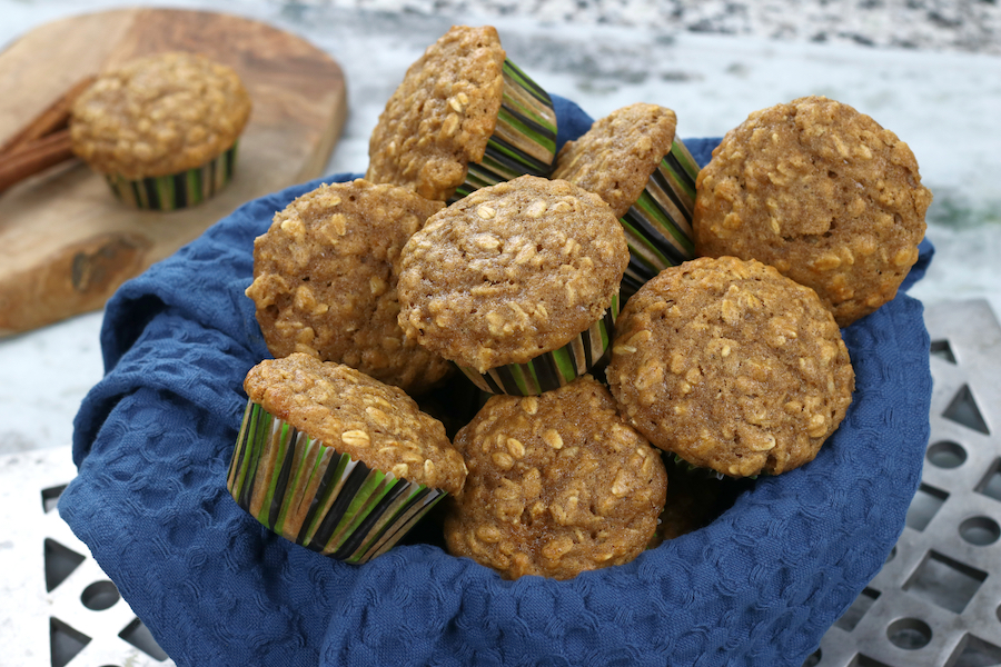 Apple Sauce Oatmeal Muffins in a blue towel lined bowl sitting on a white marble countertop.