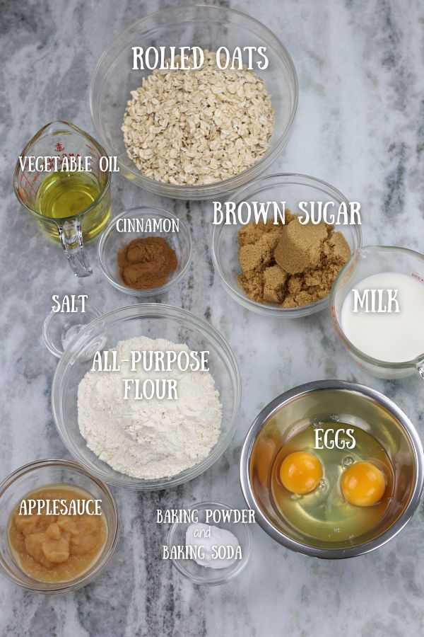Ingredients for Oatmeal Cinnamon Muffins measured into small bowls and place on a white marble countertop.