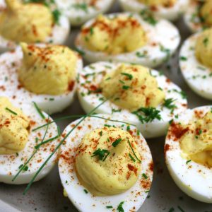 Prepared Classic Deviled Eggs Recipe lined up on a tan plate.