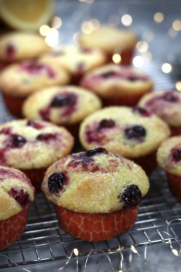 Cranberry Muffins with Fresh Cranberries on a cooling rack with out of focus white lights in background.