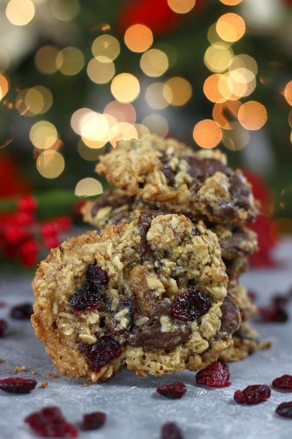 Crispy Oatmeal Coconut Cookies stacked in front of out of focus Christmas lights.