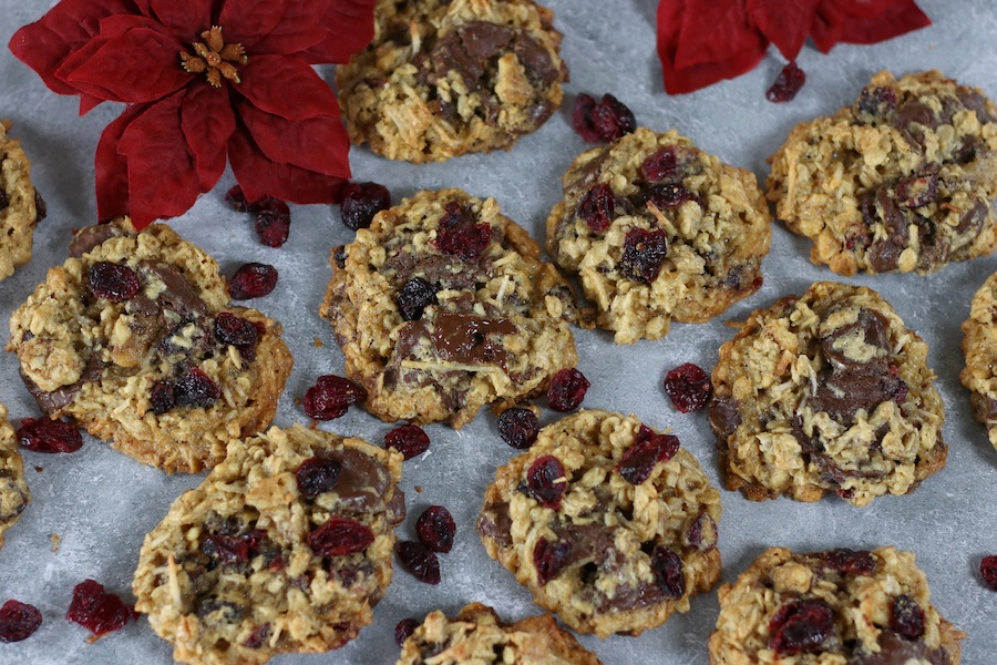 Overhead photo of Crispy Oatmeal Cookies laid in a single layer with dried cranberries and a poinsettia flower.