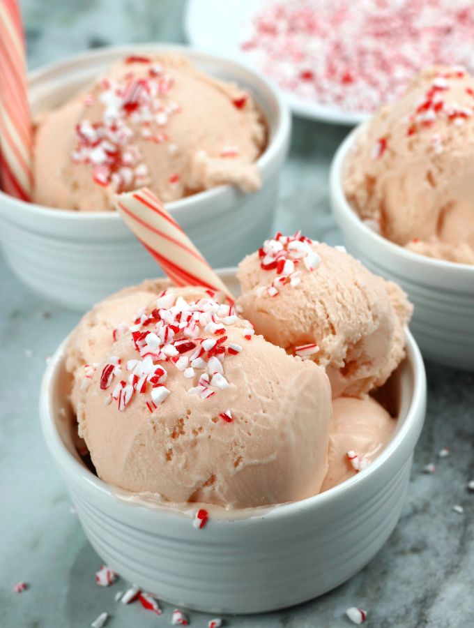 Three bowls of Peppermint Ice Cream with crushed candy canes and a peppermint stick.