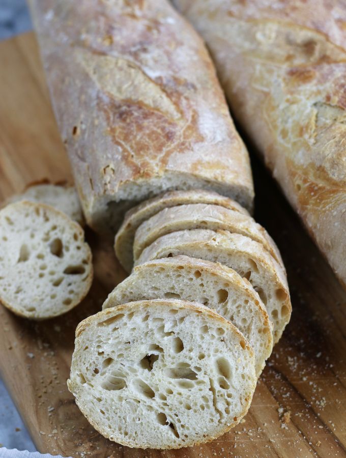 Sourdough French Bread halfway sliced on a cutting board.