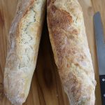 Two Sourdough French Loaves on a wooden cutting board sitting next to a bread knife.