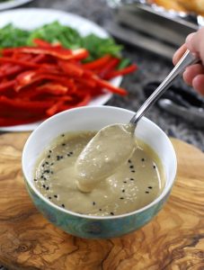 A bowl containing Miso Tahini Dressing, with a spoonful poised over the bowl.