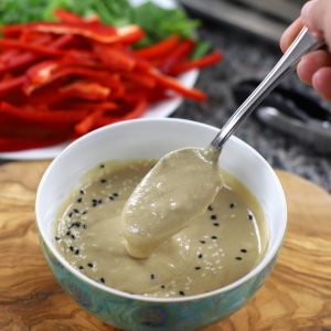 A bowl containing Miso Tahini Dressing, with a spoonful poised over the bowl.