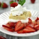 Simple recipe for Strawberry Shortcake, beautifully presented on a white scalloped plate resting on a white marble countertop.