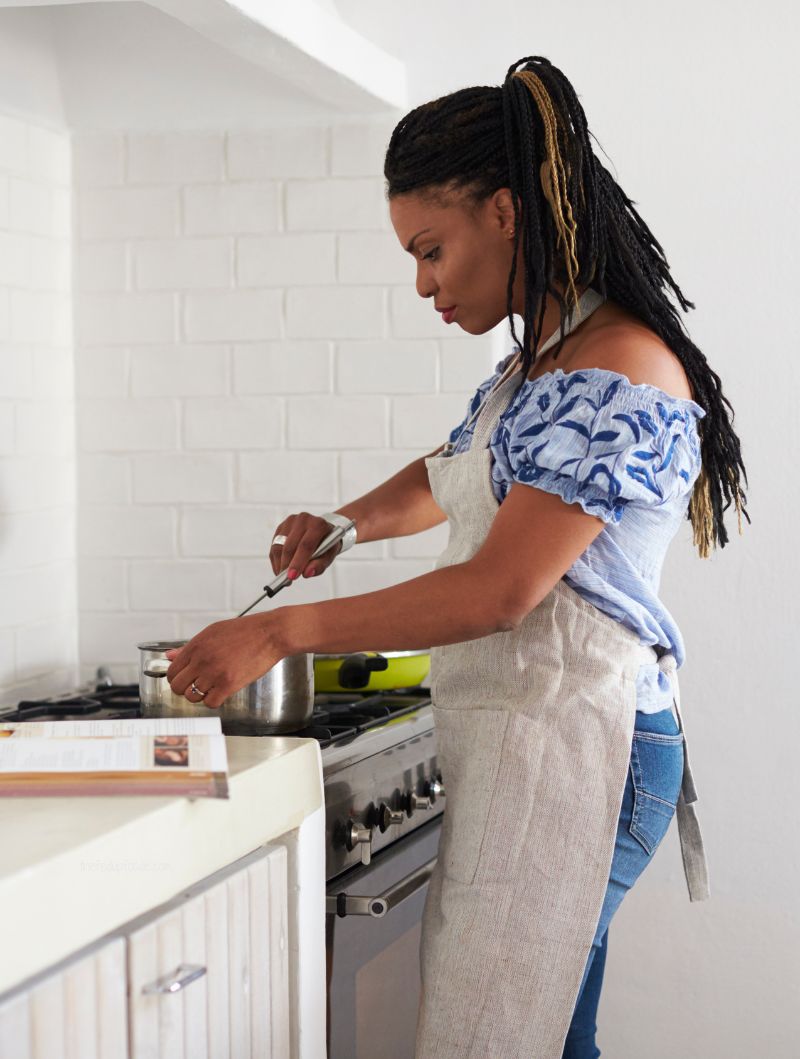 Woman following a recipe while stirring a pot on the stove in a home kitchen, representing beginner-friendly cooking tips.