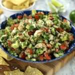 A big bowl of Shrimp Ceviche with Cooked Shrimp sitting on a wooden cutting board surrounded by chips.