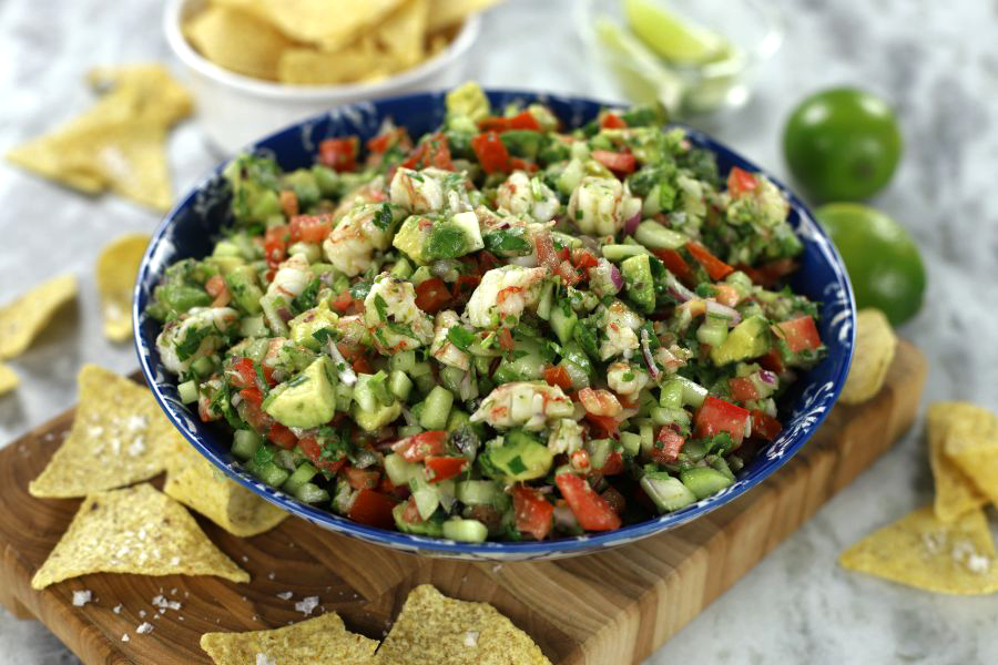 A big bowl of Shrimp Ceviche with Cooked Shrimp sitting on a wooden cutting board surrounded by chips.