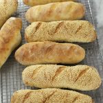 Several Sourdough Sub Rolls lined up on a cooling rack.